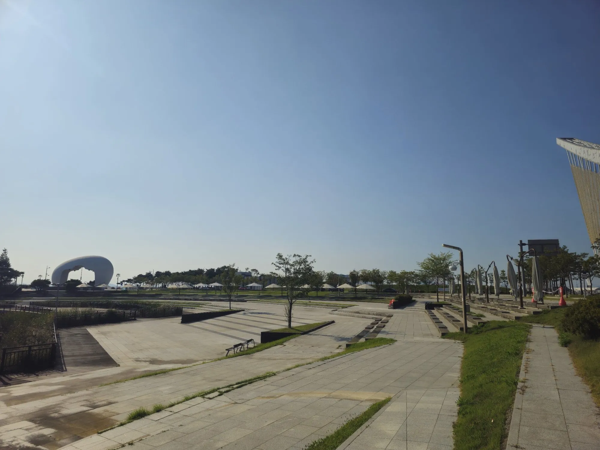 Jeongseojin plaza in morning light, with the white Sunset Bell sculpture on the left and the Ara Tower's frame at the right edge.